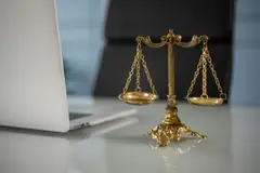Golden justice scales on a desk beside a laptop
