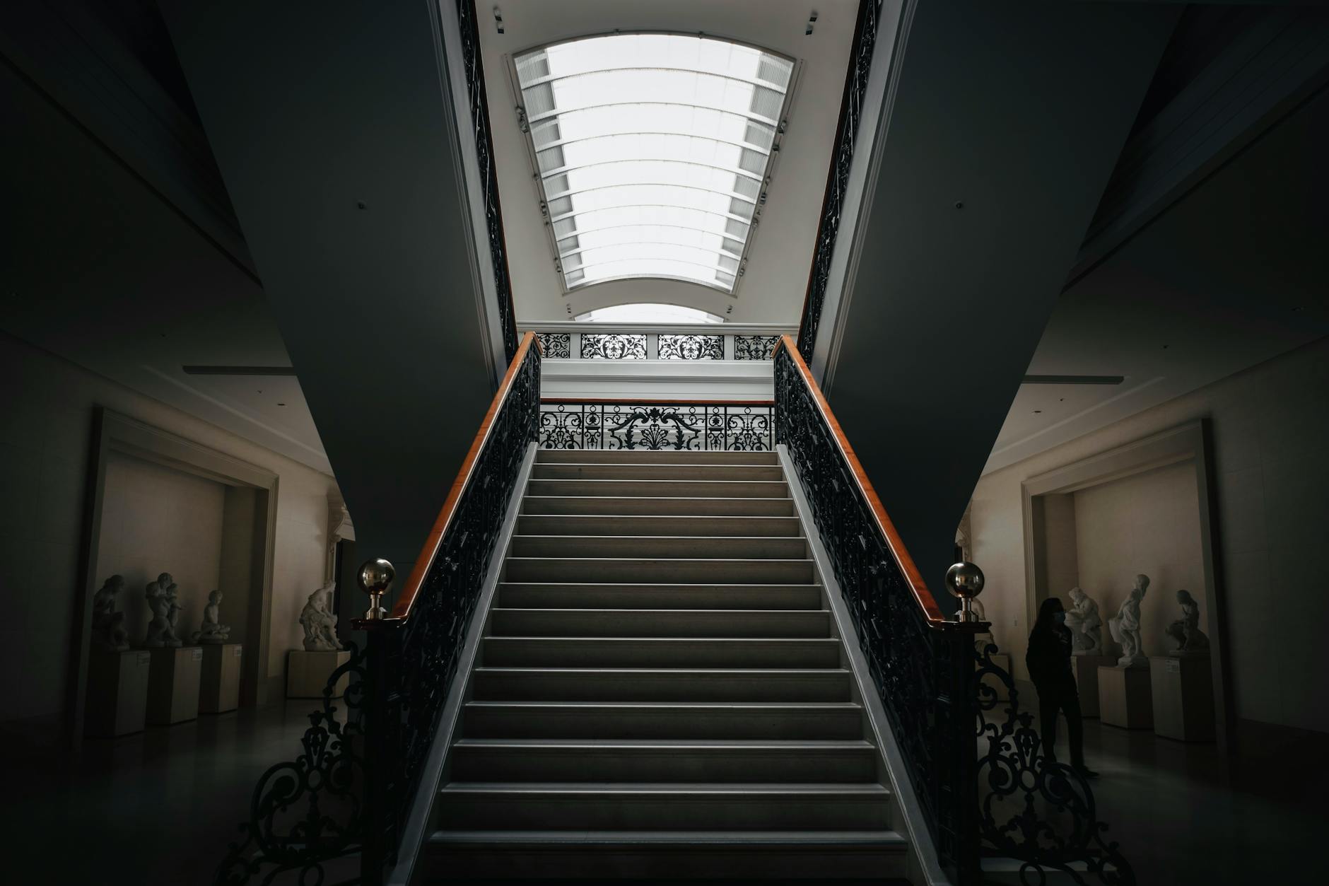 A dimly lit museum hallway with stairs and sculptures